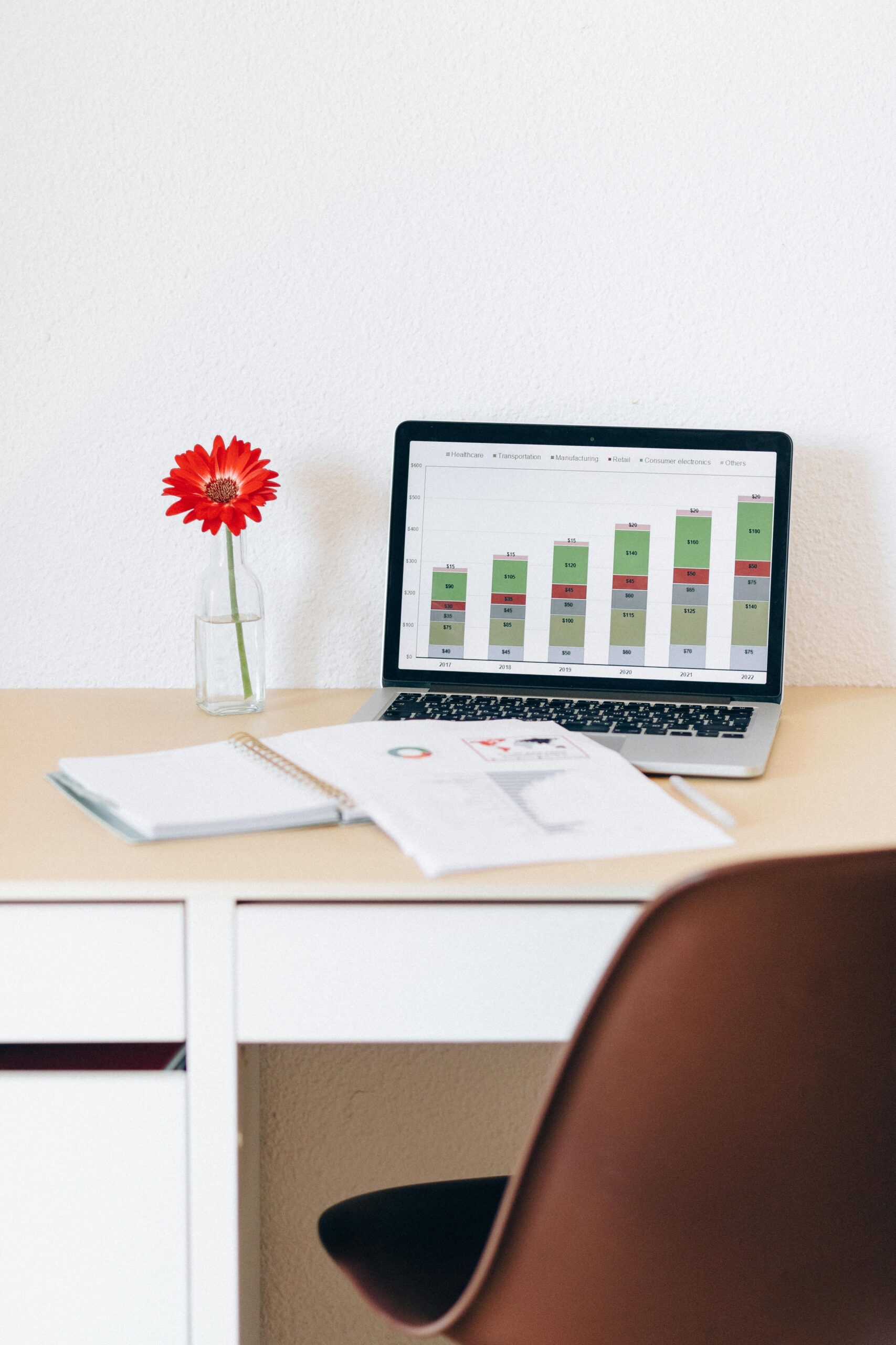 Modern home office with laptop displaying financial charts and a red flower in a vase for a touch of style.